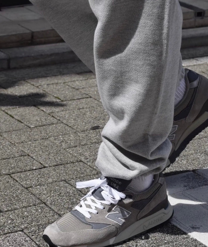 Grey low-top sneakers on feet with white laces, worn with light grey pants
