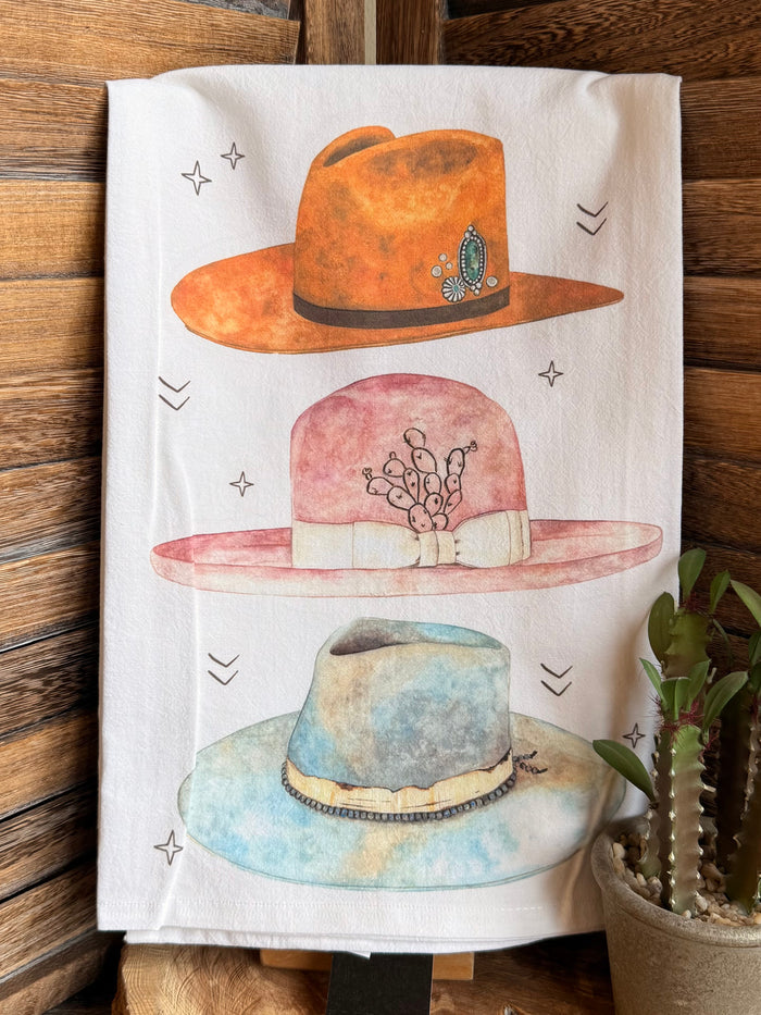White tea towel featuring stacked watercolor hats in orange, pink, and blue