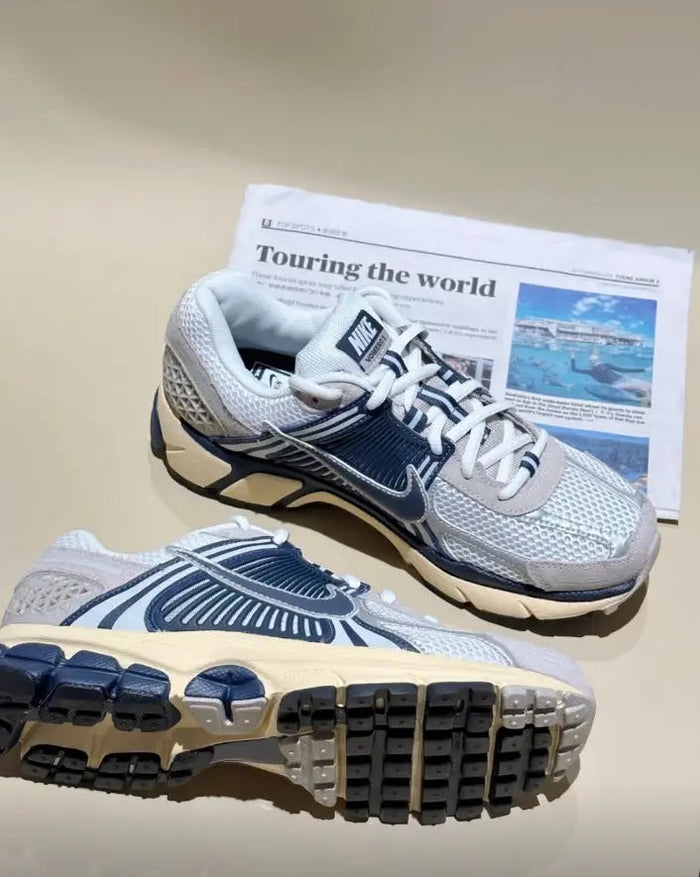 Nike running sneaker pair on book cover, light gray mesh uppers, navy swoosh, tan midsole