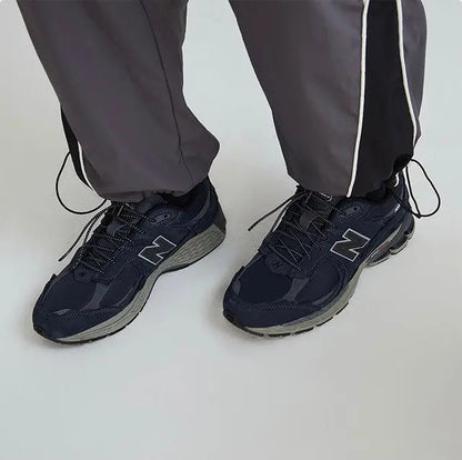 Pair of navy New Balance 2002R sneakers with N logo, worn with track pants
