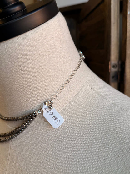 Triple layer stack chain necklace close-up, silver-toned links with small charm tag