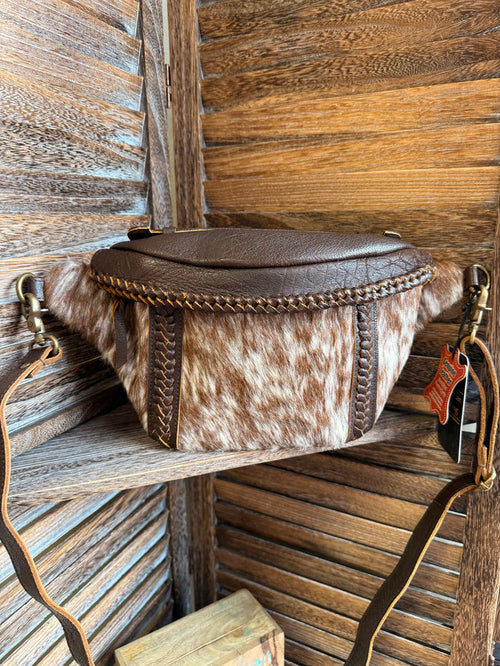 Hair-on cowhide fanny pack with brown top, braided trim, and adjustable crossbody strap