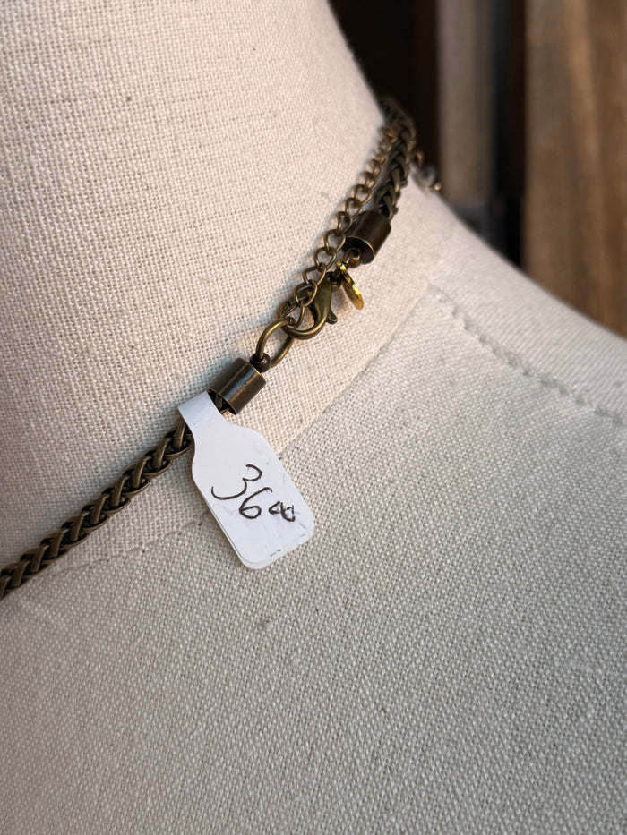 Antique brass-tone chain necklace detail with small tag and layered crystal charm links