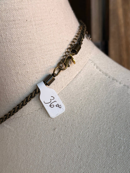 Antique brass-tone chain necklace detail with small tag and layered crystal charm links