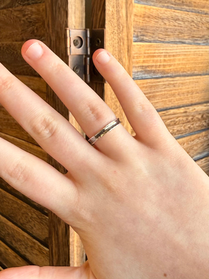 Hammered sterling silver ring on finger, slim band with glossy textured surface