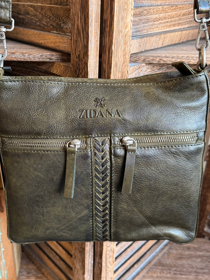 Olive leather crossbody bag close-up: center braided zipper and two side pockets, logo patch.