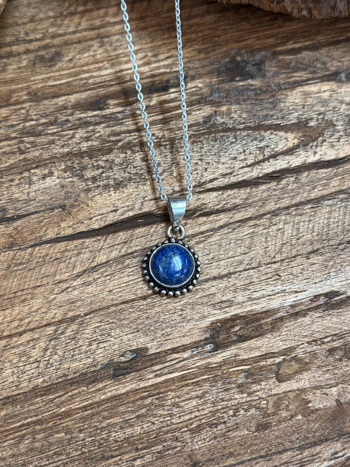 Silver chain necklace with round lapis-blue cabochon pendant and halo border