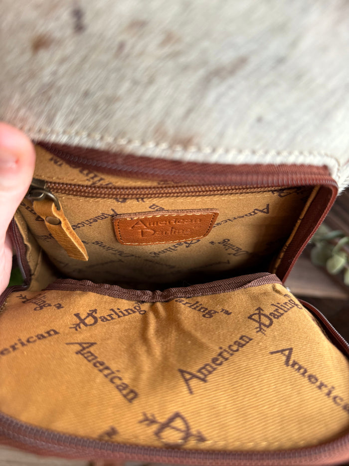 Open hair-on sling backpack showing tan patterned interior lining and zipper