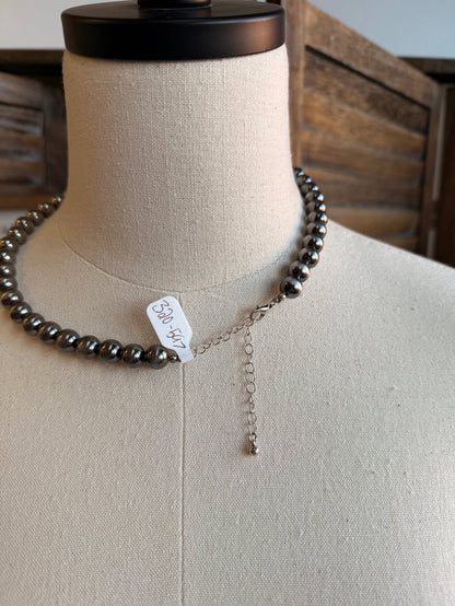 Silver pearl bead necklace with hanging chain and small stamped tag near clasp