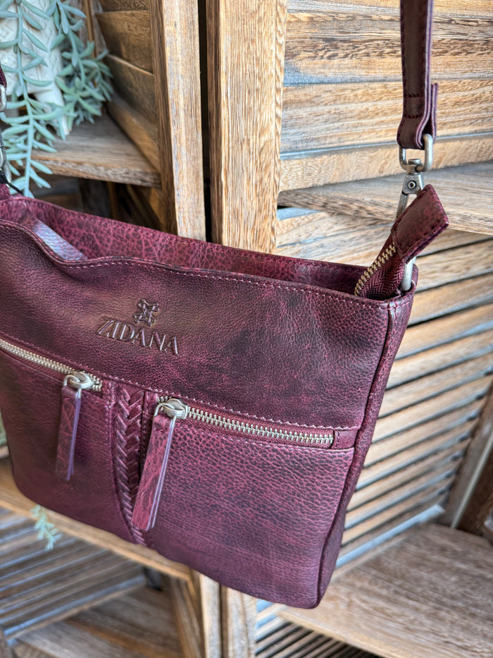 Plum double-pocket leather crossbody bag at an angle with shoulder strap and zips