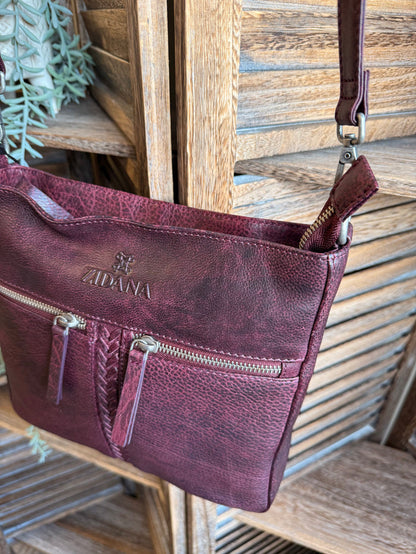 Plum double-pocket leather crossbody bag at an angle with shoulder strap and zips
