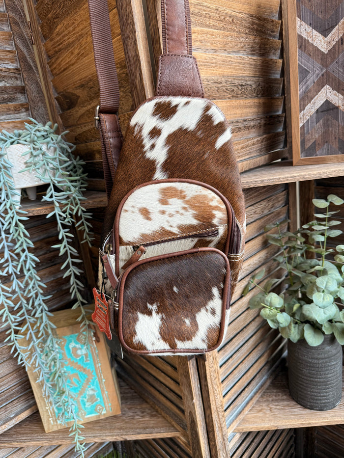 Cowhide sling bag with brown leather trim and cow-print front pockets