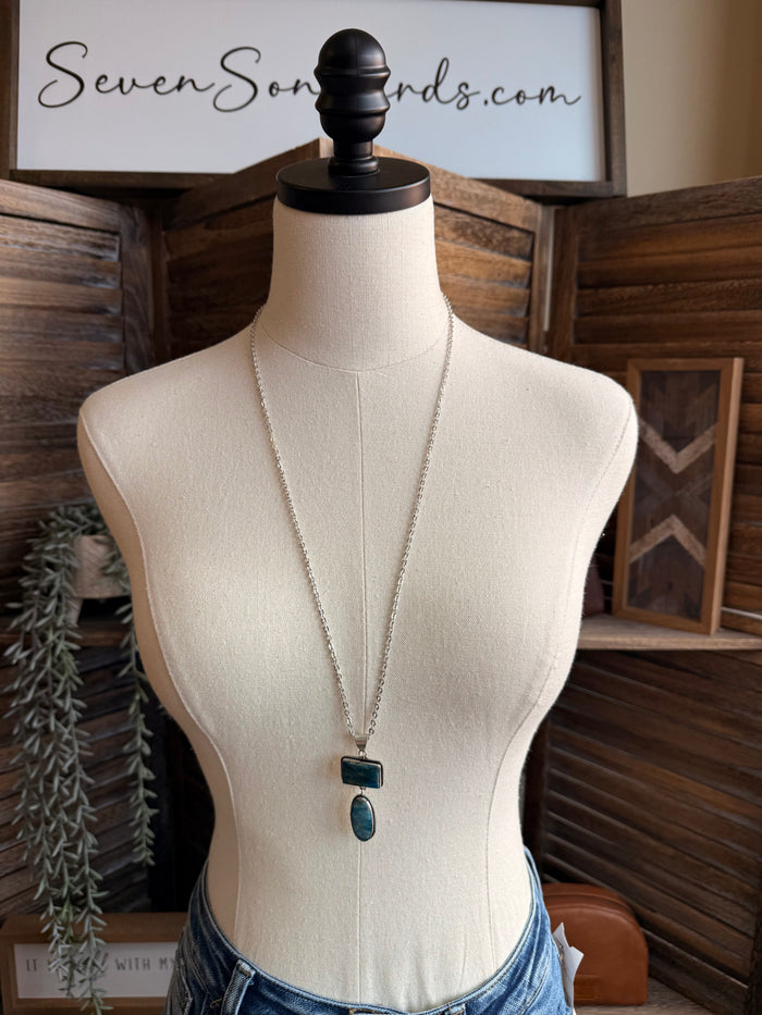 Silver lariat necklace draped on a mannequin with blue rectangular and oval pendants