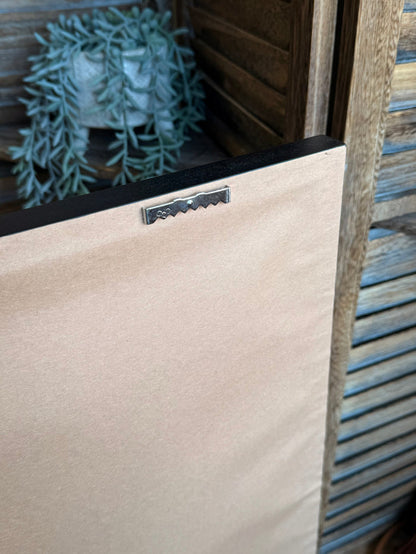 Framed artwork corner with metal latch clasp on cream backing