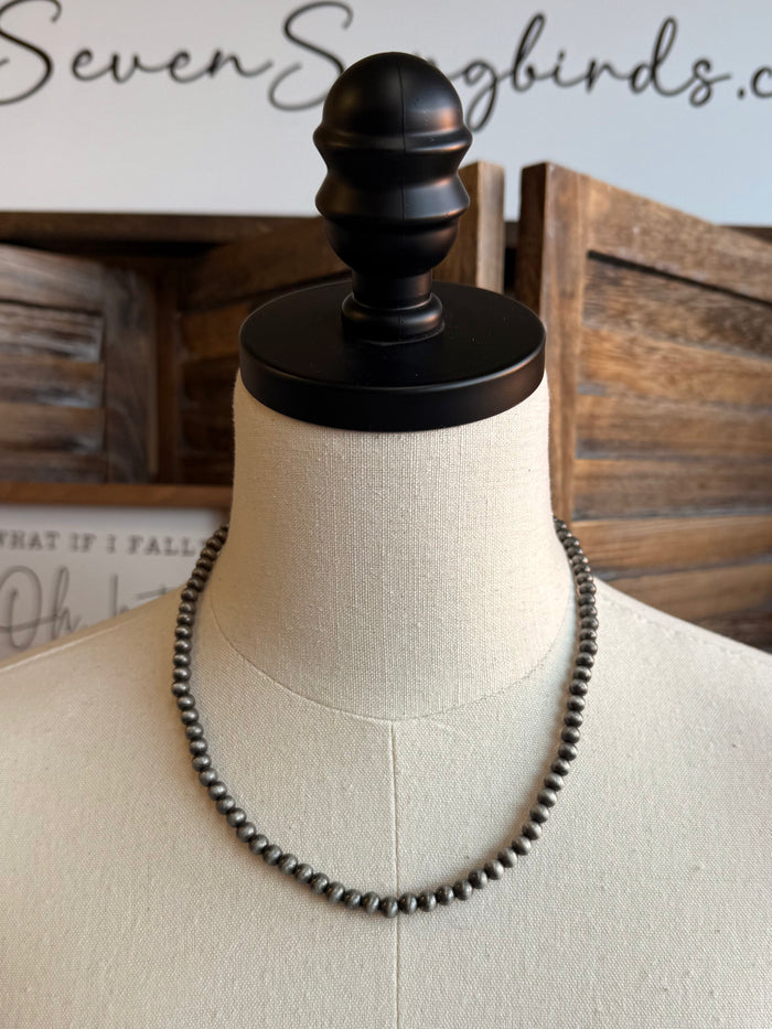 Silver pearl bead necklace with short drop charm and metal tag, mannequin view
