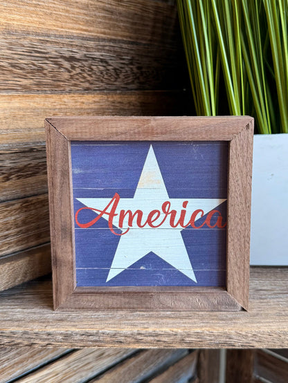 Framed blue star artwork with red America script, rustic wood 4x4 frame (angled)