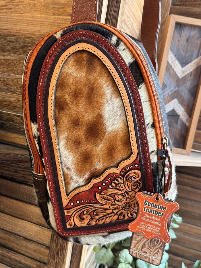 Hair-on cowhide sling bag with tan-and-brown hide front, tooled leather border, tags