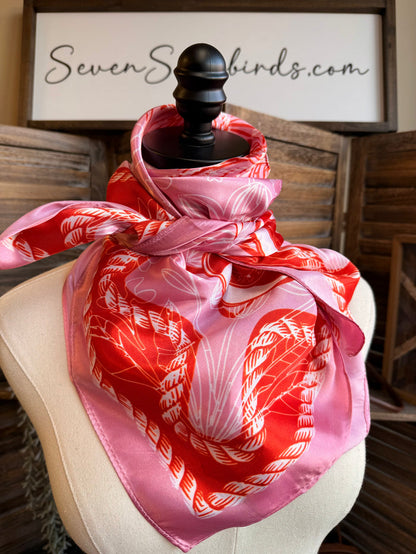Pink wild rag scarf folded with red-orange border and rope-patterned heart design.