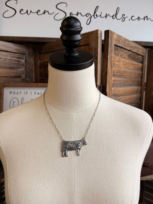 Silver-tone cow pendant necklace with chain on display bust