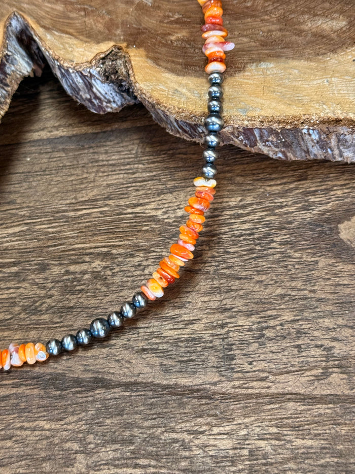 Close-up of orange spiny oyster chips with silver-tone bead necklace strand