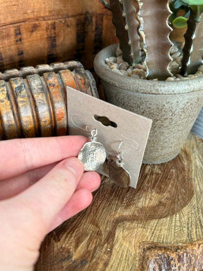 Sterling silver fishhook earring with hammered round slab disc, held up by hand