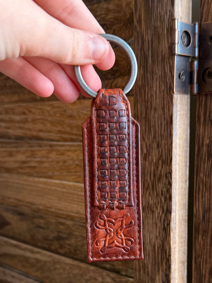 Rusty brown braided-style leather keychain tag with embossed grid and emblem, metal key ring