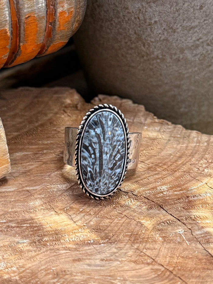 Silver-tone adjustable ring featuring an oval dark fossil stone cabochon in a beaded bezel