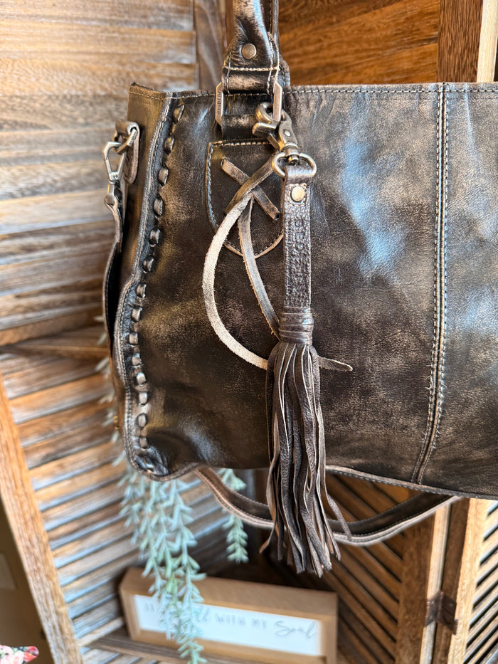Leather tassel clip with braided cords and hanging fringe on a leather tote
