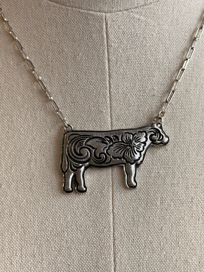Silver-tone engraved cow pendant necklace on woven fabric, close-up