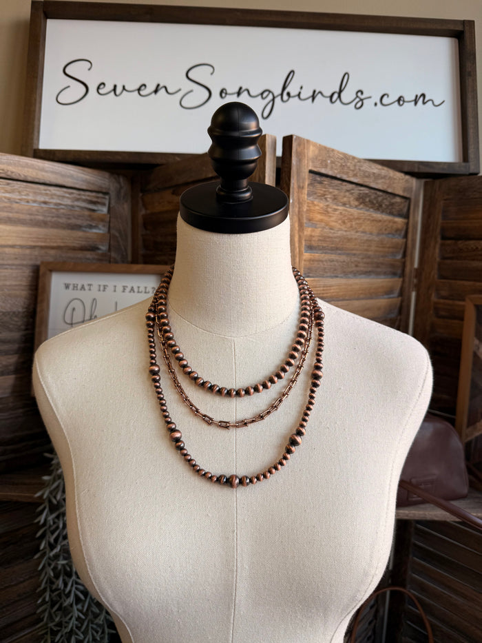 Triple pearl stack necklace with copper-tone beaded chain, three layered rows on mannequin