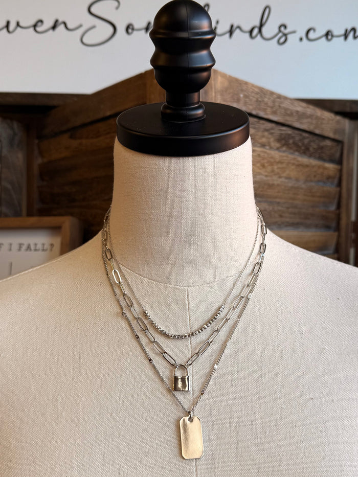 Triple-layer silver necklace with three chains, square lock charm, and rectangular plate pendant