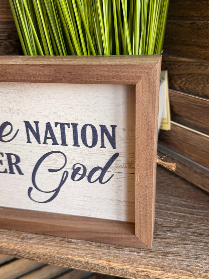 Framed artwork close-up with "Nation" and "God" lettering in blue, wood frame
