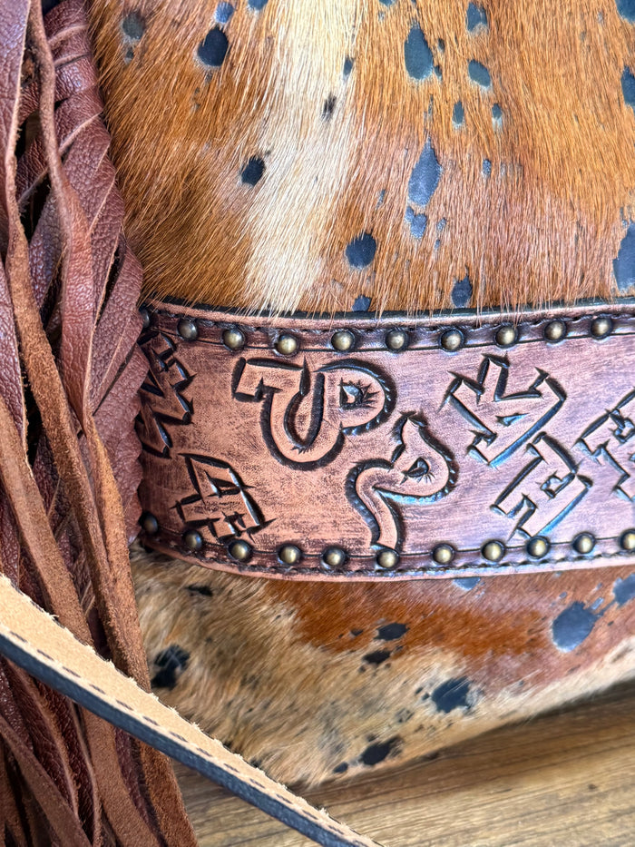 Fringed cowhide crossbody purse side detail with speckled hide, embossed band, fringe tassel