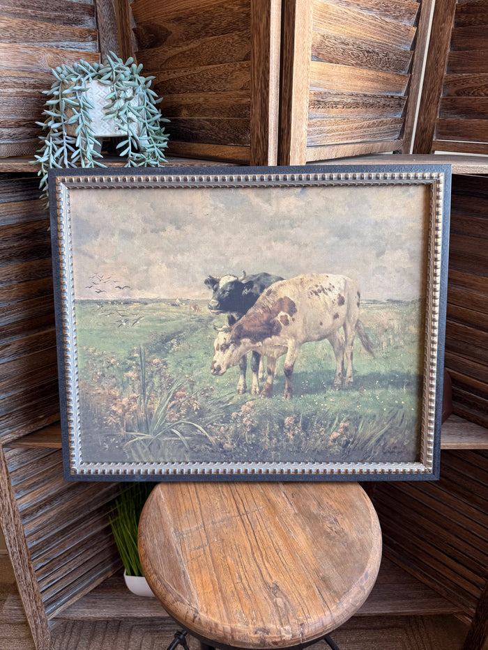 Framed prairie artwork with two cows grazing, blue bead trim around the border