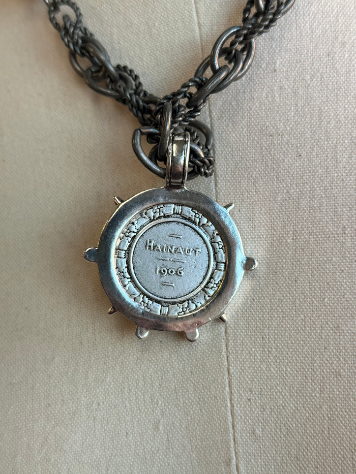 Blue-toned coin medallion charm with crystal center on dark link chain