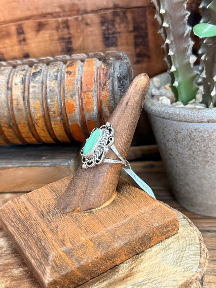 Turquoise oval sterling silver ring with filigree setting and blue tie, angled on stand
