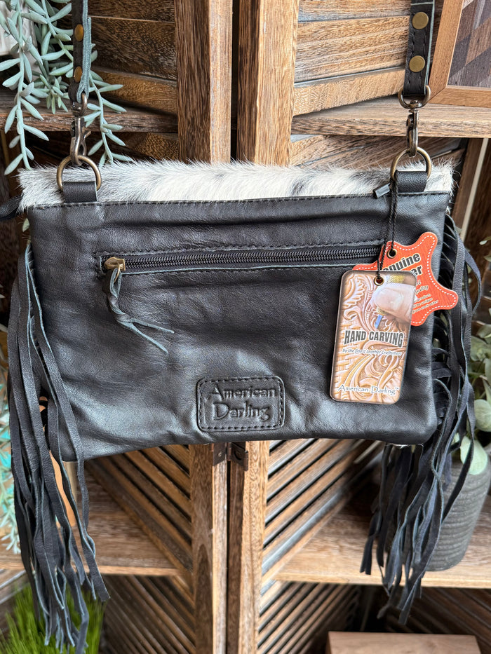 Black cowhide crossbody clutch with zipper pocket, stitched logos, fringe, and charm