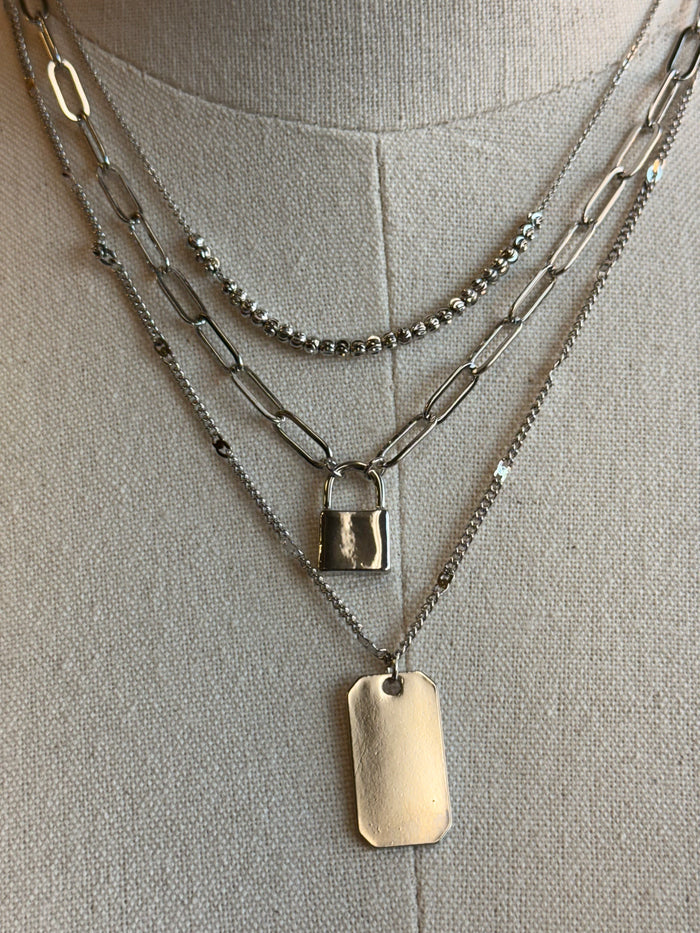Triple-layer lock necklace close-up: square lock charm and plate pendant on layered chains