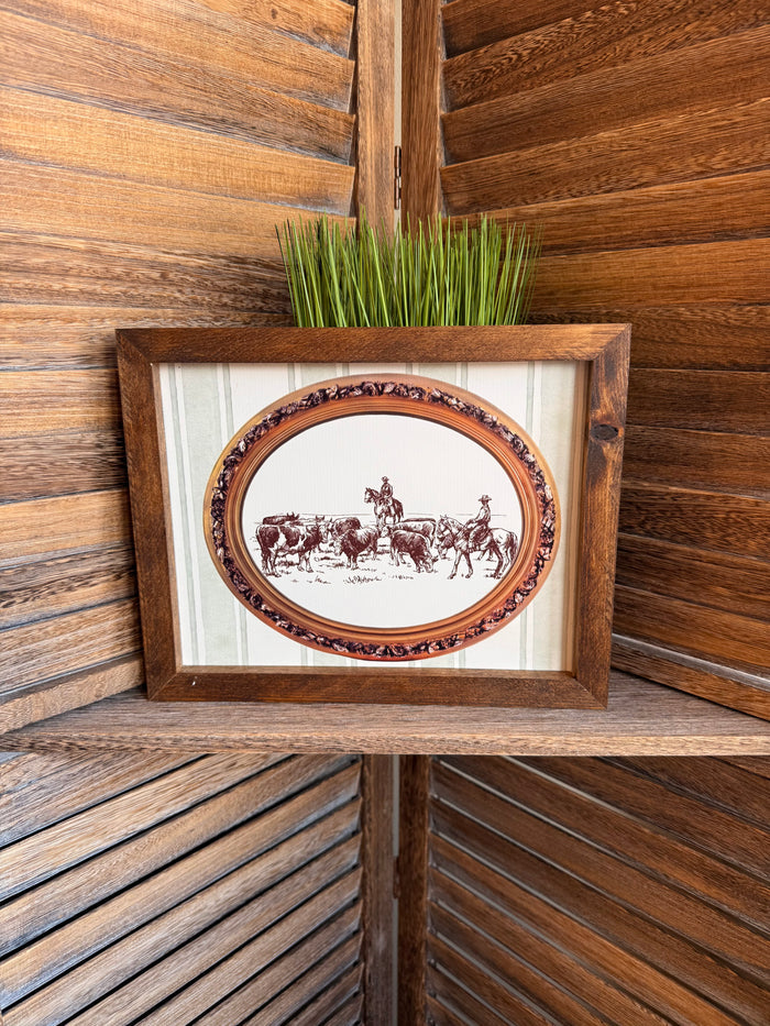 Framed oval cattle drive artwork with ornate border and distressed wood frame