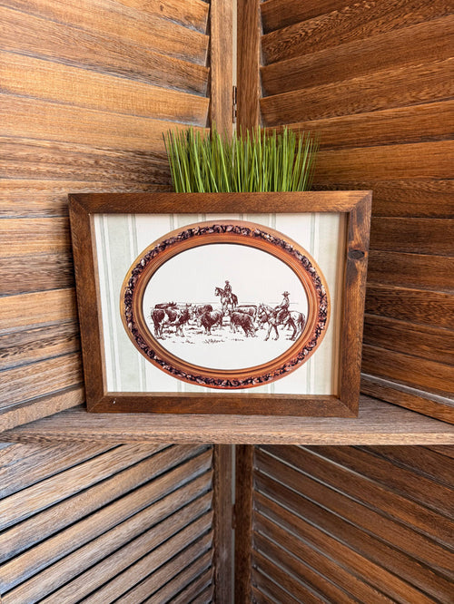Framed oval cattle drive artwork with ornate border and distressed wood frame