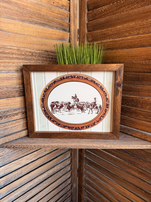 Framed oval cattle drive artwork with ornate border and distressed wood frame