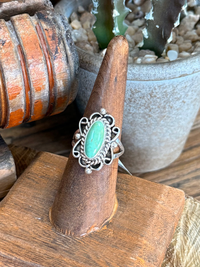 Turquoise oval sterling silver ring with decorative filigree band, side view on stand