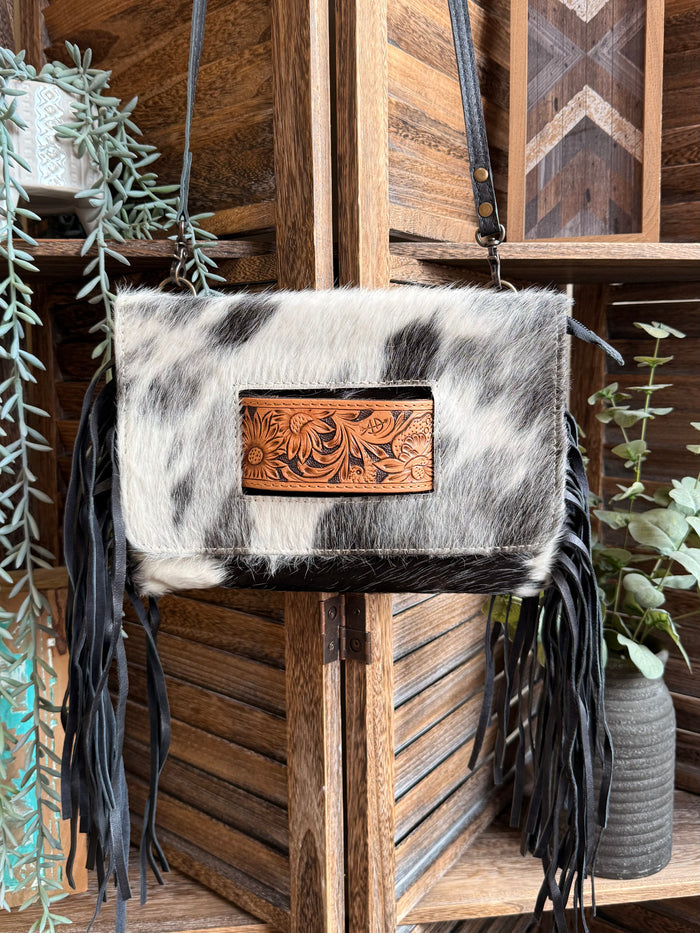 Black-and-white cowhide crossbody clutch with fringed sides and top metal chain strap