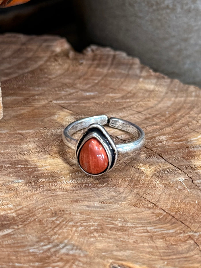 Adjustable silver-toned ring showing red oval gemstone in a teardrop bezel