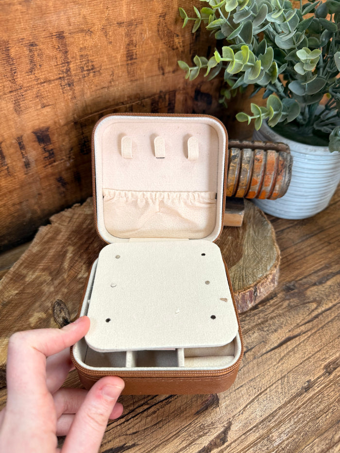 Beige travel jewelry box open showing inner slots and peg dividers