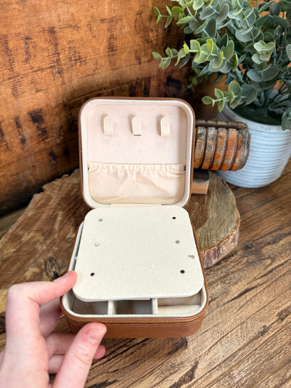 Beige travel jewelry box open showing inner slots and peg dividers