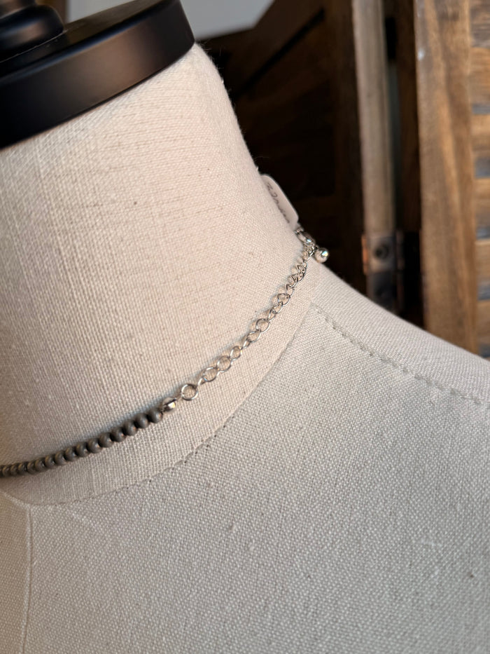 Silver-tone chain necklace detail with close-up of checker bar pendant