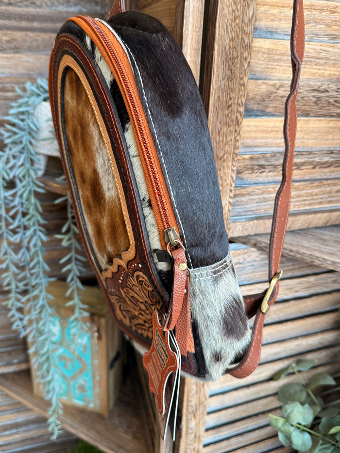 Cowhide sling bag side view with dark fur panel, tooled leather detail, zip