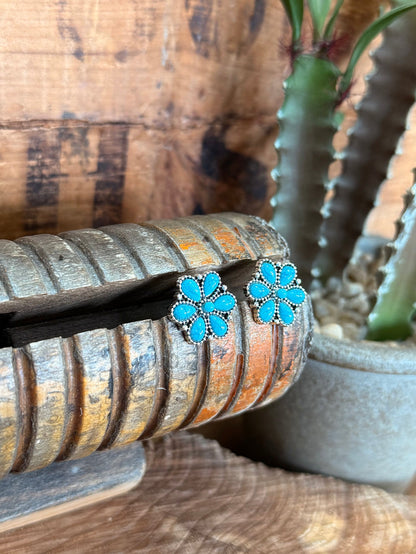 Small turquoise floral stud earrings with silver border, close-up on the earring face