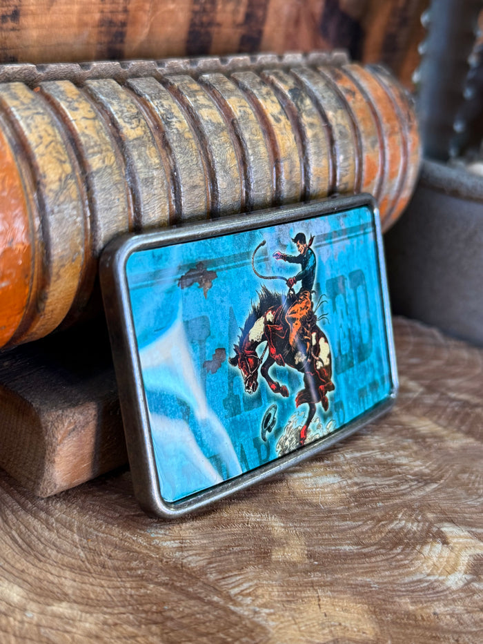 Cowboy saddle bronc belt buckle angled, blue rider-on-bronc graphic, silver frame